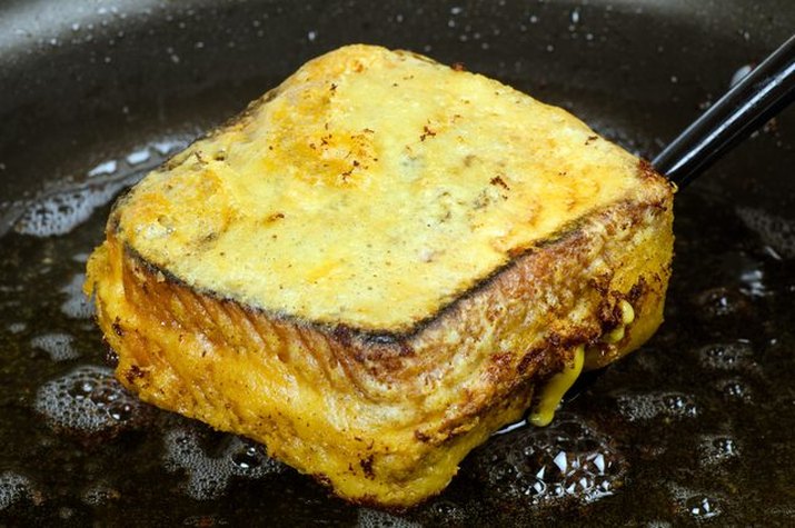 A freshly deep-fried grilled cheese sandwich emerging from hot oil.