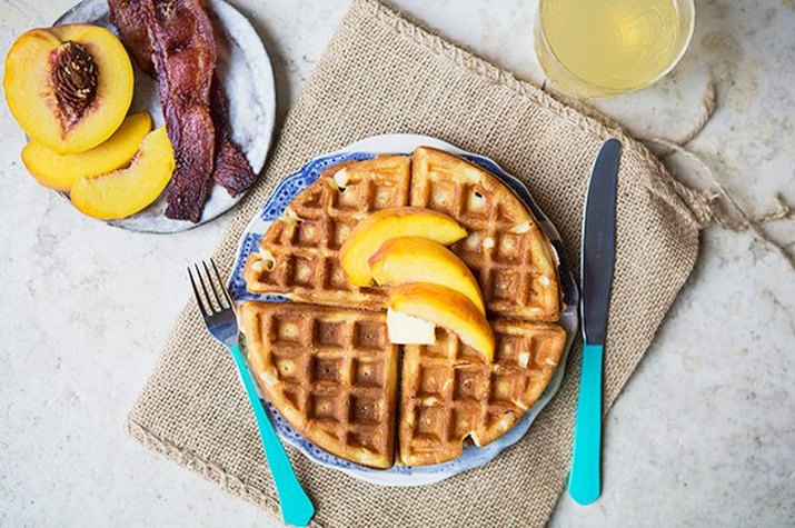 Short stack of waffles covered with peaches and maple syrup.