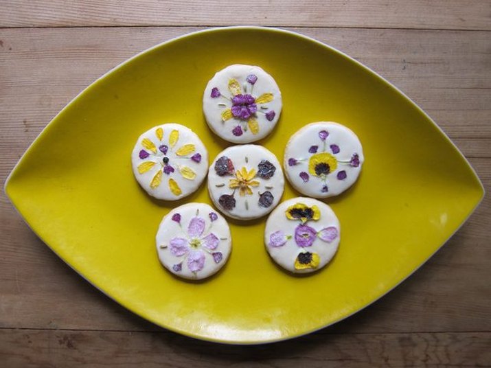 A plate of frosted sugar cookies decorated with edible flowers.