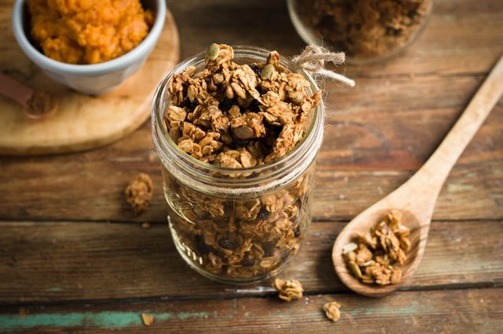 A mason jar full of granola next to a wooden spoon