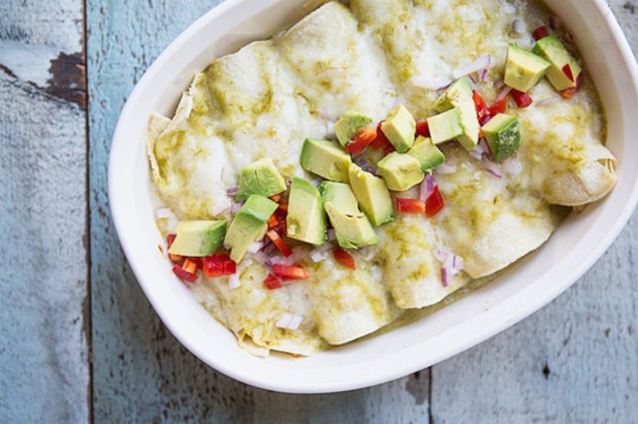 A casserole dish of enchiladas topped with diced peppers and avocados.
