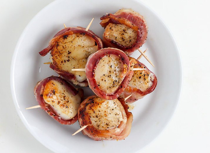 Grilled bacon-wrapped scallops on a white plate.