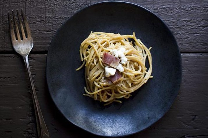 A plate of spaghetti sprinkled with caramelized onions, bacon and goat cheese.