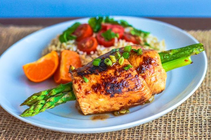 Sweet and spicy teriyaki chicken-wrapped asparagus served with rice, cherry tomatoes and orange slices.