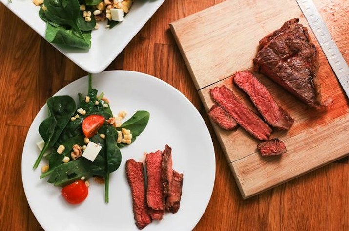 Cutting board and plate with grilled bison steak and side spinach salad.