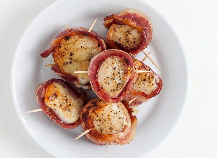Freshly grilled bacon wrapped scallops arranged on two skewers.