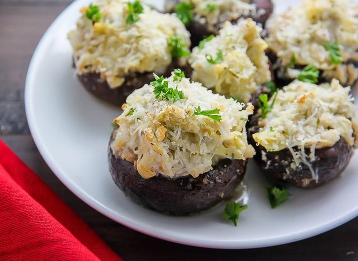 A plate of artichoke dip stuffed mushrooms garnished with parsley.