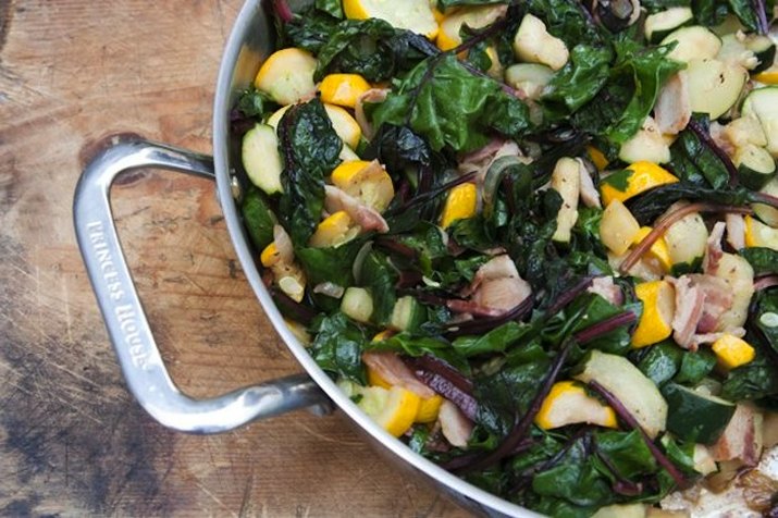 Linguini tossed with sautéed Swiss chard, summer squash and bacon in a skillet.