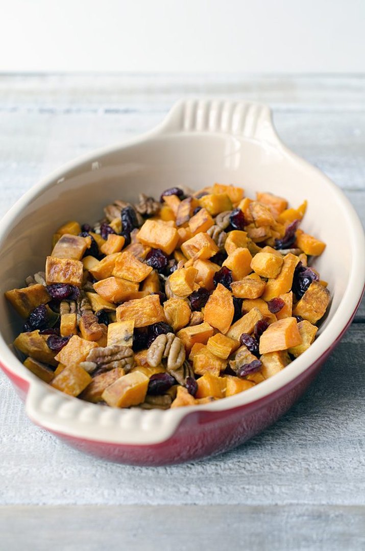 A casserole dish of roasted sweet potatoes, cranberries and pecans.
