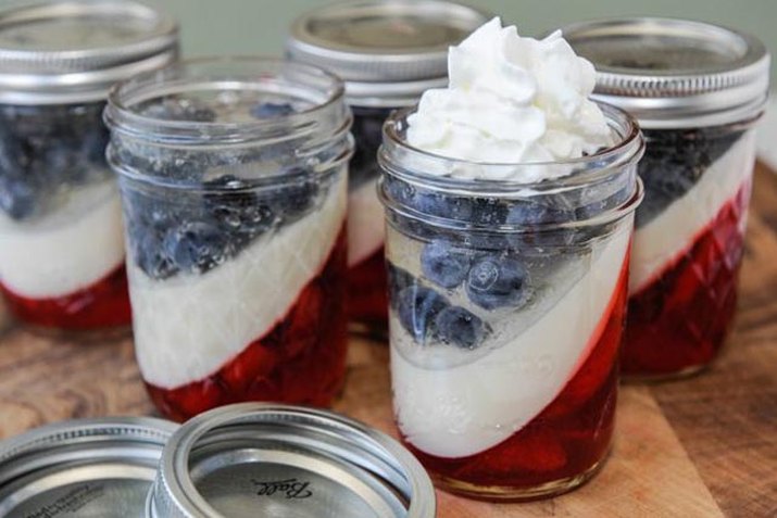 Mason jars filled with red, white and blue layers and topped with whipped cream.