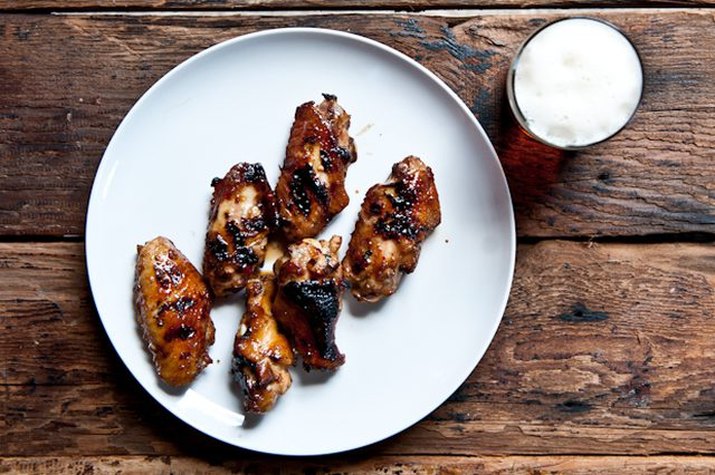 A plate of five honey glazed wings served with a glass of beer.