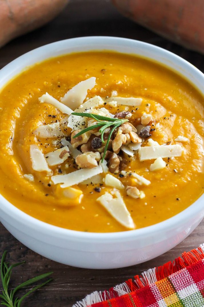 A bowl of sweet potato soup topped with cheese, nuts and rosemary.