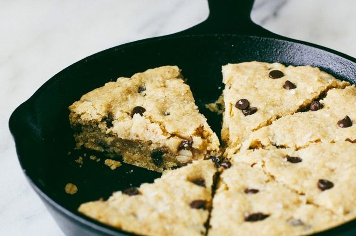 A cast iron skillet filled with a fresh and chewy chocolate chip cookie.
