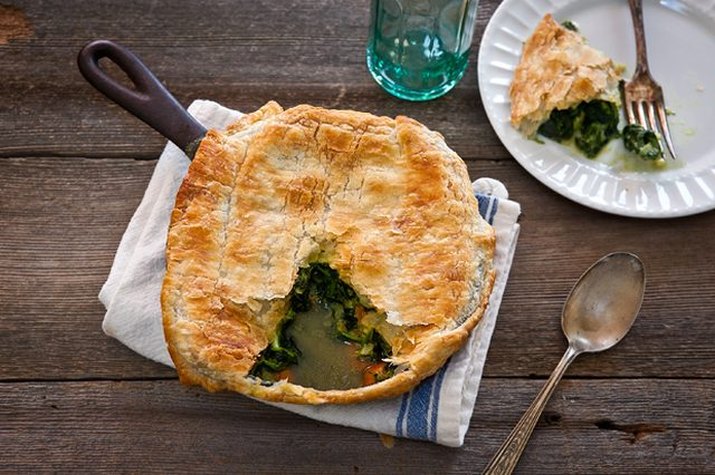 A large skillet spinach and artichoke pot pie on a wooden table