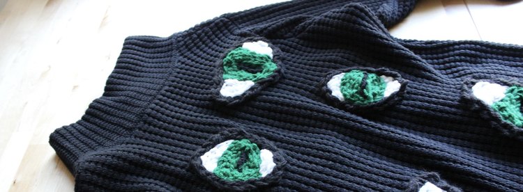 Closeup of black knit sweater with embroidered green cat eyes
