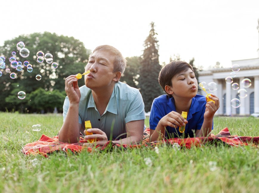 asian old father together with son lie on the grass in the park and blow soap bubbles and rejoice in summer