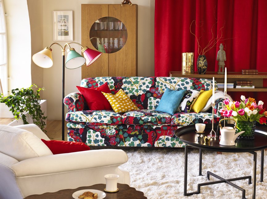 An eclectic living room with patterned couch, red curtains and a vase of tulips