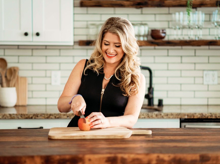 A woman in a black top with blond hair cuts an apple on a wood cutting board